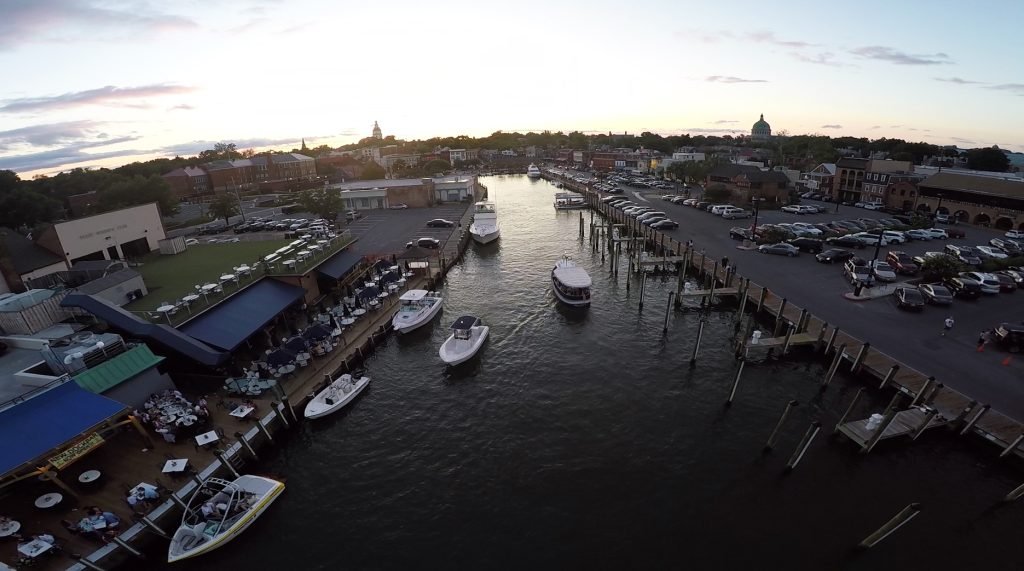 Masted sailing yachts lying along the quayside beside Dock Street in Annapolis harbour, with waterfront buildings behind them