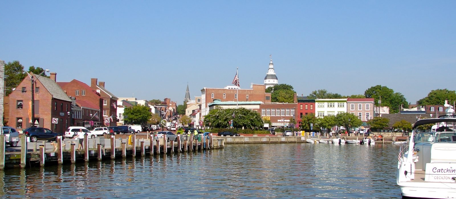Boats moored in Annapolis harbour at City Dock, with the Alex Haley memorial statues on the quay and the Maryland State House tower on the skyline behind