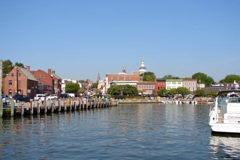 Boats moored in Annapolis harbour at City Dock, with the Alex Haley memorial statues on the quay and the Maryland State House tower on the skyline behind