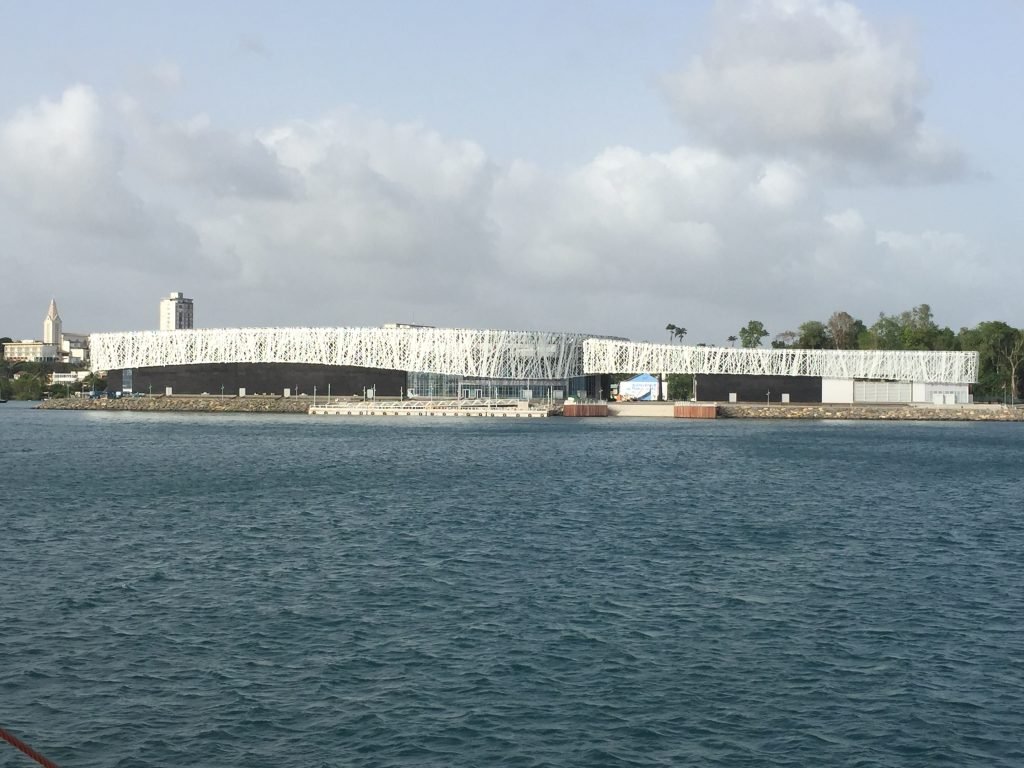 The Mémorial ACTe building on the Pointe-à-Pitre waterfront in Guadeloupe seen from the water, its silver lattice facade above a dark base
