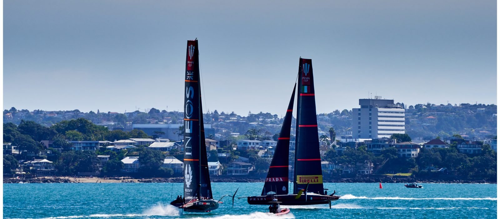 Two AC75 foiling monohulls, Luna Rossa Prada Pirelli and INEOS TEAM UK, sailing towards each other as they enter the pre-start box on flat water
