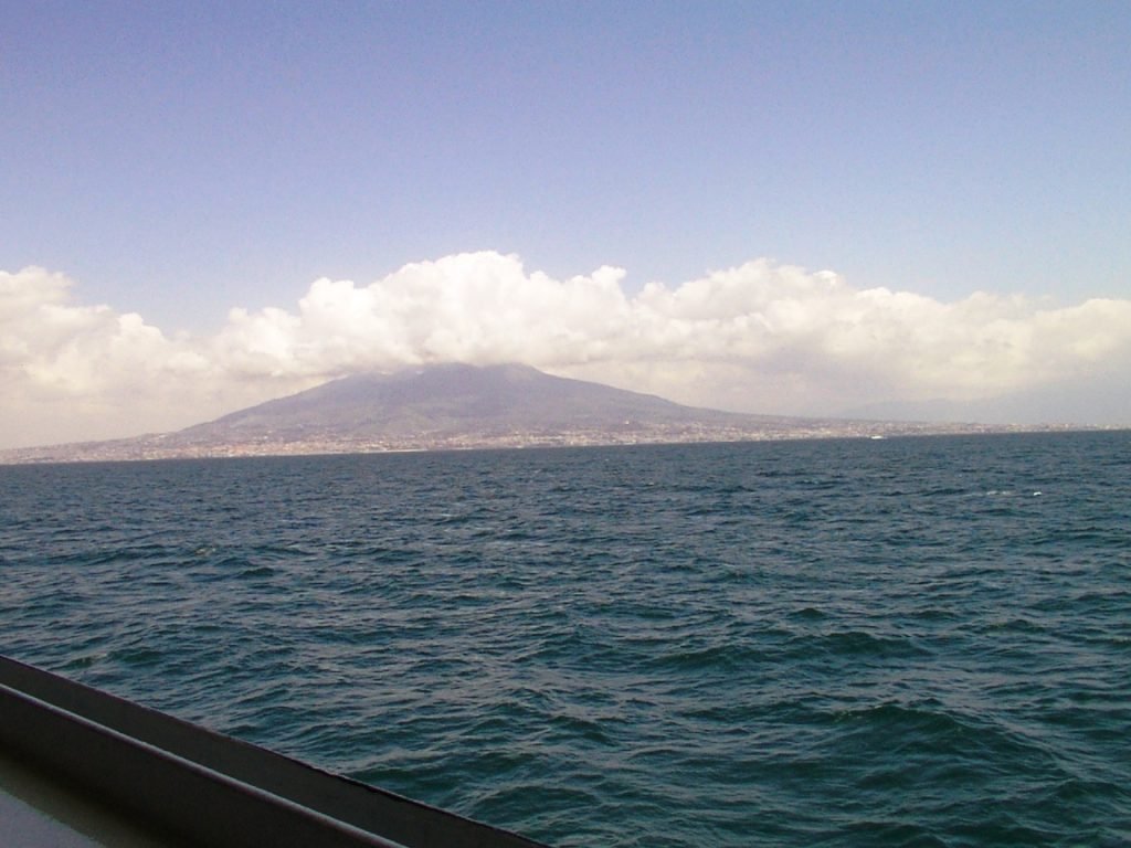 The Gulf of Naples seen from the water, with the coastline low on the horizon and the twin peaks of Mount Vesuvius rising behind it